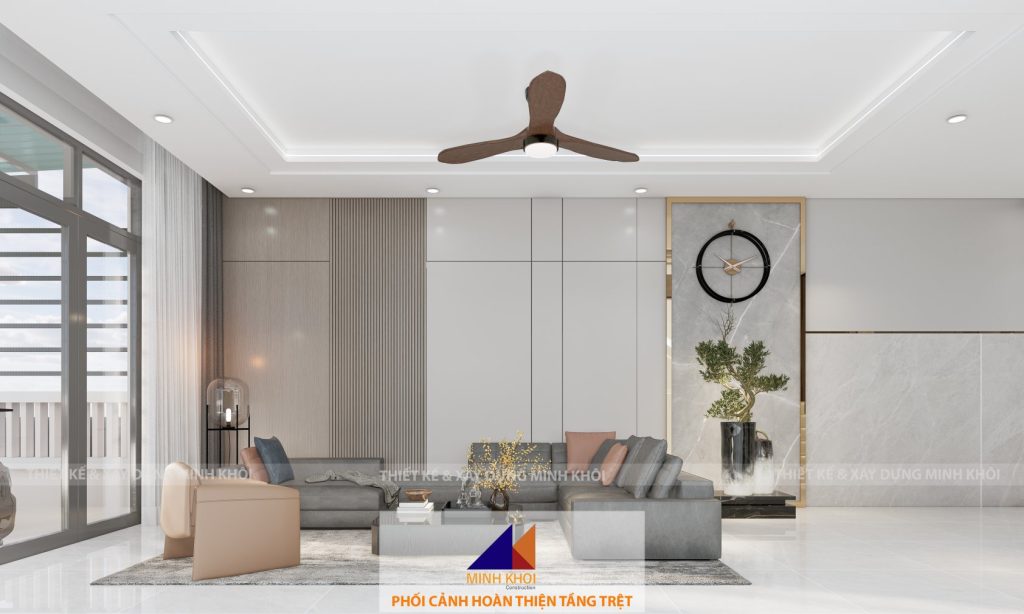 Phòng khách được thiết kế với phong cách hiện đại, tinh tế, tạo nên không gian sống ấm áp và sang trọng. Tông màu chủ đạo là trắng và xám, kết hợp với điểm nhấn từ chất liệu gỗ nâu tự nhiên, mang lại cảm giác hài hòa và thanh lịch. Không gian mở: Cửa kính lớn đón ánh sáng tự nhiên, giúp không gian trở nên thoáng đãng và gần gũi với thiên nhiên. Hệ thống rèm cửa hai lớp linh hoạt, vừa đảm bảo ánh sáng vừa giữ sự riêng tư cho gia đình. Nội thất: Bộ sofa góc màu xám nhạt sang trọng, kết hợp cùng bàn trà nhỏ gọn với mặt kính đen. Chiếc ghế đơn màu be nhấn mạnh sự mềm mại, bổ sung thêm sự thoải mái cho không gian tiếp khách. Kệ tivi thiết kế âm tường, giúp tối ưu hóa diện tích và tăng tính thẩm mỹ. Trang trí: Đồng hồ treo tường độc đáo với khung vàng ánh kim nổi bật trên nền tường ốp gỗ và đá. Chậu cây và bình hoa nhỏ làm tăng nét tự nhiên, mềm mại cho tổng thể không gian. Hệ thống ánh sáng: Đèn âm trần và đèn chiếu sáng bổ sung được bố trí hợp lý, tạo nên ánh sáng dịu nhẹ và đều khắp căn phòng. Quạt trần tích hợp đèn hiện đại vừa mang tính năng động vừa tiết kiệm diện tích. Tất cả các yếu tố trên đã được Công ty Xây dựng Minh Khôi thiết kế và hoàn thiện với sự tận tâm và tỉ mỉ, mang đến cho gia chủ một không gian phòng khách hoàn hảo để sinh hoạt và đón tiếp bạn bè, người thân.